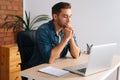 Side view of thinking handsome freelance programmer male in wireless earphone working on laptop computer sitting at desk Royalty Free Stock Photo