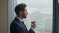 Side view thoughtful businessman drinking coffee at office window close up.