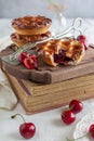 Side view of three individual cherry pies on a wooden board on top of a stack of books with fresh cherries around and serving Royalty Free Stock Photo
