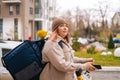 Side view of tired food delivery woman with thermo backpack holding mobile phone waiting next order standing with