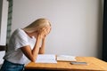 Side view of tired blonde young woman massaging temples, suffering from headache after paperwork, sitting at desk with Royalty Free Stock Photo