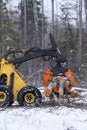 Small stand-on mini skid steer with grapple full of wooden logs
