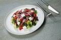 Traditional Greek salad on marble plate served with fork and knife on stone background