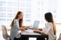 Side view of two businesswomen discussing new project sharing ideas sitting at desk opposite each other in office room Royalty Free Stock Photo