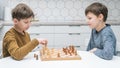 Side view of two focused preteen boys friends brothers sitting at white table, playing chess on wooden board, competing. Royalty Free Stock Photo