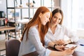 Side view of two friendly young business women working using digital tablet at meeting desk with job documents at office Royalty Free Stock Photo