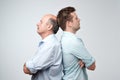 Side view of two serious men father and son standing back to back against a white background