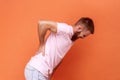 Side view of unhealthy sick man standing and holding his painful back, suffering from terrible pain. Royalty Free Stock Photo