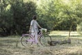 Side view of unrecognizable back looking young long haired man holding a pink vintage cute bike in the park Royalty Free Stock Photo