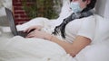 Side view of unrecognizable ill Caucasian man in coronavirus face mask lying on bed couching and talking using video