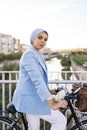 Side view of a muslim woman standing with her bike on a footbridge looking at camera Royalty Free Stock Photo