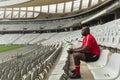 Upset African American Male rugby player sitting with rugby ball in stadium