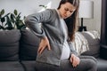 Side view of upset pregnant young female suffering lower back pain sitting on sofa in living room. Sad future mother suffer from Royalty Free Stock Photo