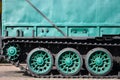 Side view of the vehicle on a caterpillar track with black tracks and green wheels and a side metal wal