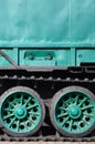 Side view of the vehicle on a caterpillar track with black tracks and green wheels and a side metal wal