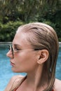 Side view vertical portrait of confident sexy woman in pool looking away. Woman with wet hair wearing sunglasses and red Royalty Free Stock Photo