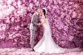 Side view of wedding couple kissing white standing against wall covered with pink flowers