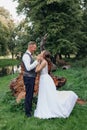 Side view of wedding couple standing near roots of fallen tree in park interlacing fingers. Young woman raising one leg. Royalty Free Stock Photo