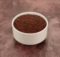 Side view of a white bowl filled with red quinoa on a maroon tabletop Royalty Free Stock Photo