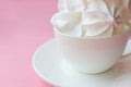 Side view on white meringues in a white teacup on a white plate on a pink background Royalty Free Stock Photo