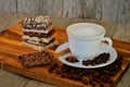 Side view of a white porcelain cappuccino cup standing on a wooden cutting board.  A stack of chocolate pieces of various kinds Royalty Free Stock Photo