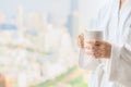 Side view of woman in bathrobe standing near the window while holding white cup of coffee and enjoy wonderful morning in the hotel Royalty Free Stock Photo