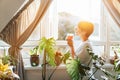 Side view woman drinking tea and looking at the sunrise or sunset while standing at the window in a room with green Royalty Free Stock Photo