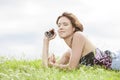 Side view of woman listening to music through MP3 player using headphones while lying on grass against sky Royalty Free Stock Photo