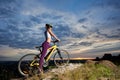 Side view woman with perfect figure on bicycle enjoying superb blue sky with clouds and sun at sunset