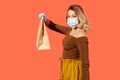 Side view woman in protective mask giving paper bag and looking at camera, advertise of food purchase Royalty Free Stock Photo