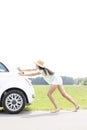 Side view of woman pushing broken down car on country road Royalty Free Stock Photo