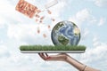 Side view of woman`s hand holding ipad with green grass growing on screen and little planet Earth on top, and plastic Royalty Free Stock Photo