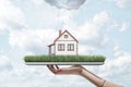 Side view of woman`s hand holding tablet with green grass and little detached house on screen, with rain cloud above Royalty Free Stock Photo