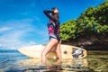 side view of woman in wetsuit with surfboard posing in ocean at Nusa dua Beach