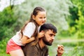 Side view of wonderful family sitting on picnic in park forest around trees. Little daughter sitting on fathers back.