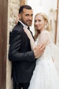 Side view of wonderful wedding couple standing on street, looking at camera. Young woman bride embracing with groom. Royalty Free Stock Photo