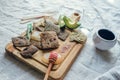 Side view of a wooden serving board with crispy linen breads, honey, green onions, pink himalaya salt, two slices of avocado, a