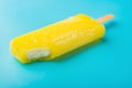 Side view yellow popsicle with a bite on blue background