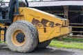Side view of a yellow road roller that\'s on the stand by mode without the roll at a park