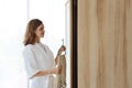 Side view young active and beautiful caucasian woman in white sleepwear choosing clothes in wooden wardrobe. Cute girl standing in