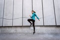 Young adult athlete woman jumping up against wall outdoor