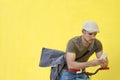 Side view of a young adult man with a vintage bike and wearing casual clothes and sunglasses standing against a yellow wall while Royalty Free Stock Photo