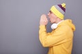 Side view of young adult man wearing yellow hoodie and beanie hat posing isolated over gray background, screaming with hands near Royalty Free Stock Photo