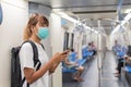 Side view of young Asian backpacker woman wear face mask holding smartphone travel to the city by subway or Skytrain, COVID-19 Royalty Free Stock Photo