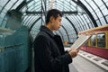 Side view of young Asian businessman intently reading newspaper while waiting train at metro station Royalty Free Stock Photo