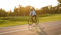 Side view of a young athletic man in sportswear cycling in city park at sunset, riding mountain road bike