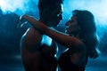 side view of young attractive woman in bra hugging sexy muscular mixed race man on blue with smoke. Royalty Free Stock Photo