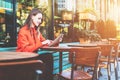 Side view. Young attractive woman in orange coat is sitting outside in cafe at table and uses tablet computer. Royalty Free Stock Photo