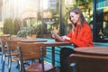 Side view. Young attractive woman in orange coat is sitting outside in cafe at table and uses tablet computer. Royalty Free Stock Photo