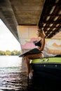 side view of attractive woman in swimsuit and with wakeboard sit on edge of boat under bridge Royalty Free Stock Photo